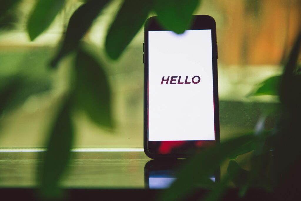 Smartphone with 'Hello' greeting on screen surrounded by green leaves, creating a fresh and tech-savvy ambiance.